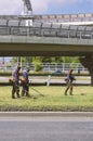 Three workers in overalls mow the grass on the lawn with trimmers