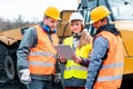 Three workers in a quarry discussing in front of heavy machinery