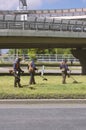 Three workers with string trimmers in orange jumpsuits mow the grass near the highway