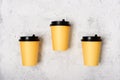 Three yellow paper cups, light gray concrete background. Minimalism concept. Place for text. Flatlay. Coffee to go