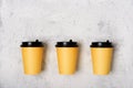 Three yellow paper cups on a light gray concrete background. Place for text from above. Copy space. Mockup. Minimalism concept.