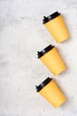 Three yellow paper cups on a light grey concrete background. Flatlay. Place for text on the left. Copy space. Minimalism concept.