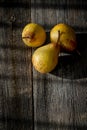 Three yellow pears on a barn wood plank table with shadows from the sun