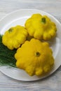 Three yellow round zucchini on a plate close-up. Fresh mini patty pan squash on a wooden table, selective focus Royalty Free Stock Photo