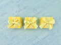 Three yellow square gift boxes in a row on blue watercolor textured background, top view. Royalty Free Stock Photo