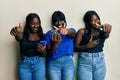 Three young african american friends using smartphone approving doing positive gesture with hand, thumbs up smiling and happy for Royalty Free Stock Photo