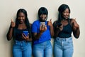 Three young african american friends using smartphone doing happy thumbs up gesture with hand Royalty Free Stock Photo