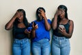 Three young african american friends using smartphone peeking in shock covering face and eyes with hand, looking through fingers Royalty Free Stock Photo