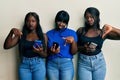 Three young african american friends using smartphone pointing down looking sad and upset, indicating direction with fingers, Royalty Free Stock Photo