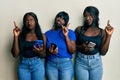 Three young african american friends using smartphone pointing up looking sad and upset, indicating direction with fingers, Royalty Free Stock Photo