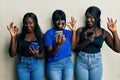 Three young african american friends using smartphone smiling positive doing ok sign with hand and fingers Royalty Free Stock Photo