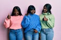 Three young african american friends wearing wool winter sweater doing happy thumbs up gesture with hand Royalty Free Stock Photo