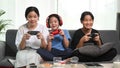 Three young girls playing video games together on sofa at home.