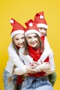 Three Young Beautiful Caucasian Ladies of Different Ages Embracing Together in Santa Hats and Cacual Clothes Against Trendy Yellow Royalty Free Stock Photo