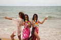 three young and beautiful latin women with a glass of blue cocktail stroll along the beach happily talking to each other and Royalty Free Stock Photo
