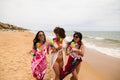 three young and beautiful latin women with a glass of blue cocktail stroll along the beach happily talking to each other and Royalty Free Stock Photo
