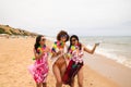 three young and beautiful latin women with a glass of blue cocktail stroll along the beach happily talking to each other and Royalty Free Stock Photo