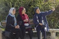 Three young beautiful muslim women in colorful hijabs are taking selfie photo. Iranian girls sitting on a park bench
