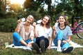 Three young beautiful women girlfriends having fun in a summer park while sitting on green grass taking off protective masks from Royalty Free Stock Photo