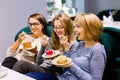 Three young beautiful Women sitting on the sofa in cafe indoors and Having lunch In Cafe. Women eating cakes and having Royalty Free Stock Photo