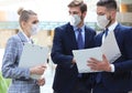 Three young businessmen wear preventive masks during epidemy, stand and discuss business at an office meeting. Royalty Free Stock Photo