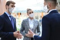 Three young businessmen wear preventive masks during epidemy, stand and discuss business at an office meeting. Royalty Free Stock Photo