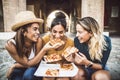 Three young female friends eating pizza sitting outside - Happy women enjoying street food in the city Royalty Free Stock Photo