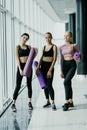 Three young fitness girls holding yoga mat while standing in gym near panoramic windows Royalty Free Stock Photo