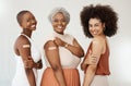 Three young friends showing a bandaid on their arms standing against a white wall together at work. Happy businesswomen Royalty Free Stock Photo