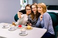 Three young friends women - three girls, sitting at a table in a cafe, chatting, smiling, drinking coffee from white Royalty Free Stock Photo
