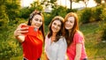 Three young girl friends taking picture of themselves on cell phone at summer sunny day. Outdoor portrait of three Royalty Free Stock Photo