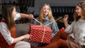 Three young girls sitting on the couch and having fun unwrapping Christmas presents at home