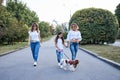 Three young girls, wearing blue jeans and white shirts, walking in city park with small dog in summer. Family fun walk with Royalty Free Stock Photo