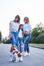 Three young girls, wearing blue jeans and white t-shirts, walking with small dog in city park in summer. Family fun leisure time Royalty Free Stock Photo