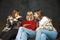 Three young happy female friends, college roommates sitting on the sofa one is holding a positive or negative pregnancy test and