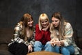 Three young happy female friends, college roommates sitting on the sofa one is holding a positive or negative pregnancy test and