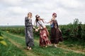 Three young hippie women, wearing boho style clothes, walking holding hands, dancing on green currant field in summer. Eco tourism Royalty Free Stock Photo