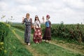 Three young hippie women, wearing boho style clothes, walking holding hands, dancing on green currant field in summer. Eco tourism Royalty Free Stock Photo