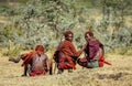 Three young Masai warriors in traditional clothes and weapons are sitting in the savannah.