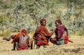 Three young Masai warriors in traditional clothes and weapons are sitting in the savannah.