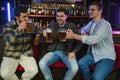 Three young men in casual clothes are smiling and clanging glasses of beer together while sitting at bar counter in pub Royalty Free Stock Photo