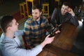 Three young men in casual clothes are smiling, holding bottles of beer while standing near bar counter in pub Royalty Free Stock Photo