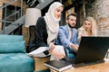Three young multiethnic business colleagues, Caucasian man and woman, Muslim lady in hijab, having conversation and Royalty Free Stock Photo
