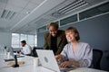 Three young multiracial business people in businesswear smiling and typing on laptop at desk in office Royalty Free Stock Photo