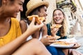 Three young multiracial women laughing while eating a piece of pizza in Italy Royalty Free Stock Photo