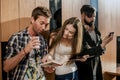 Three young people in the room. People standing near the wall with gadgets in their hands. Royalty Free Stock Photo