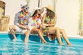 Three young people smiling sitting on the edge of a swimming pool Royalty Free Stock Photo