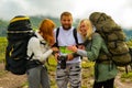 three young people of tourists friends: a guy and two girls blonde and redhead with backpacks on their back stand on a background Royalty Free Stock Photo