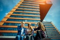 Three young pretty girlfriends sitting on bench on city street and talking. Women drink coffee from disposable glasses Royalty Free Stock Photo