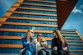 Three young pretty women sit on a bench on a city street, drinking coffee from disposable glasses, talking and laughing. Friends Royalty Free Stock Photo